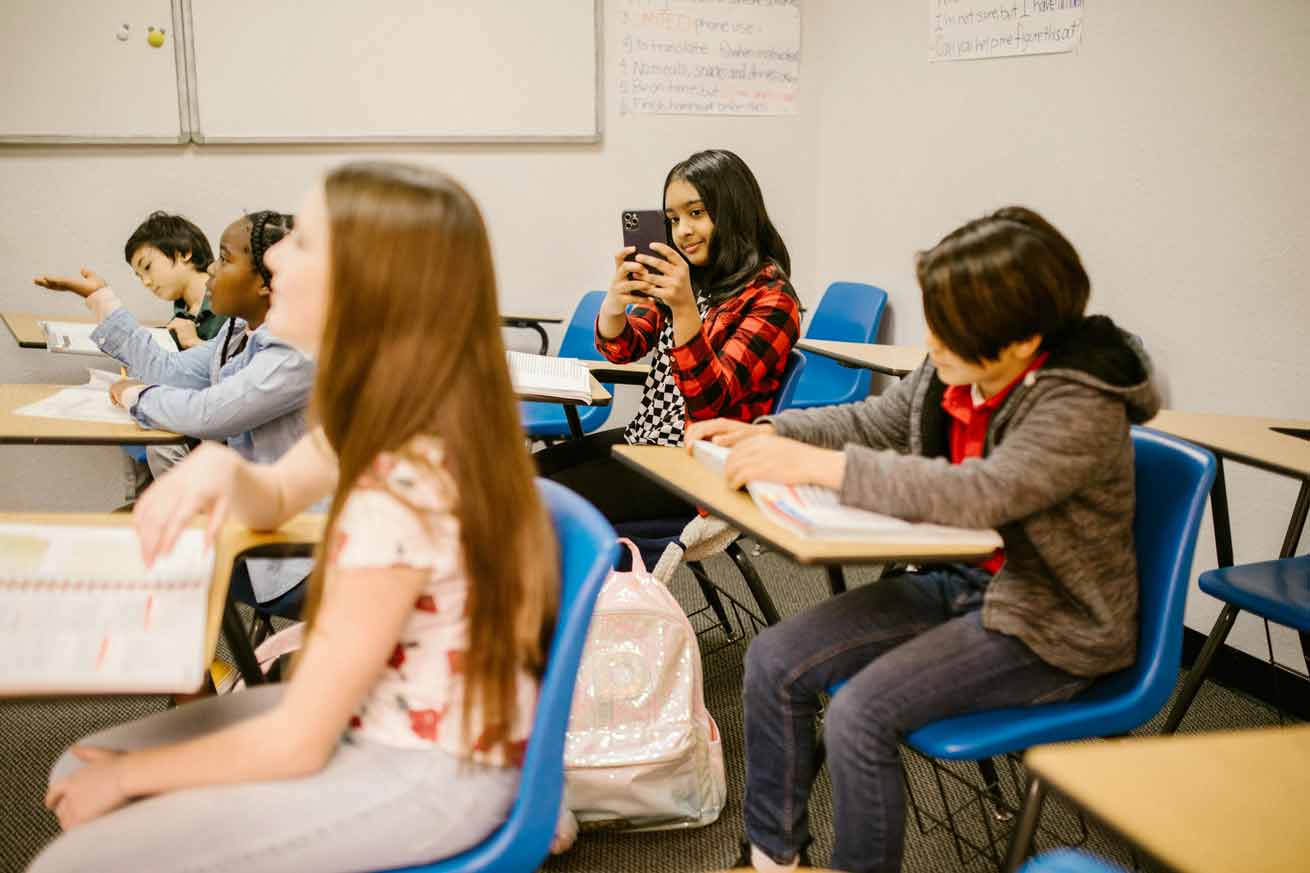 Une élève dans une classe d'école prend en photo sa camarade avec son smartphone - comment éduquer à l'ère de la distraction digitale ?